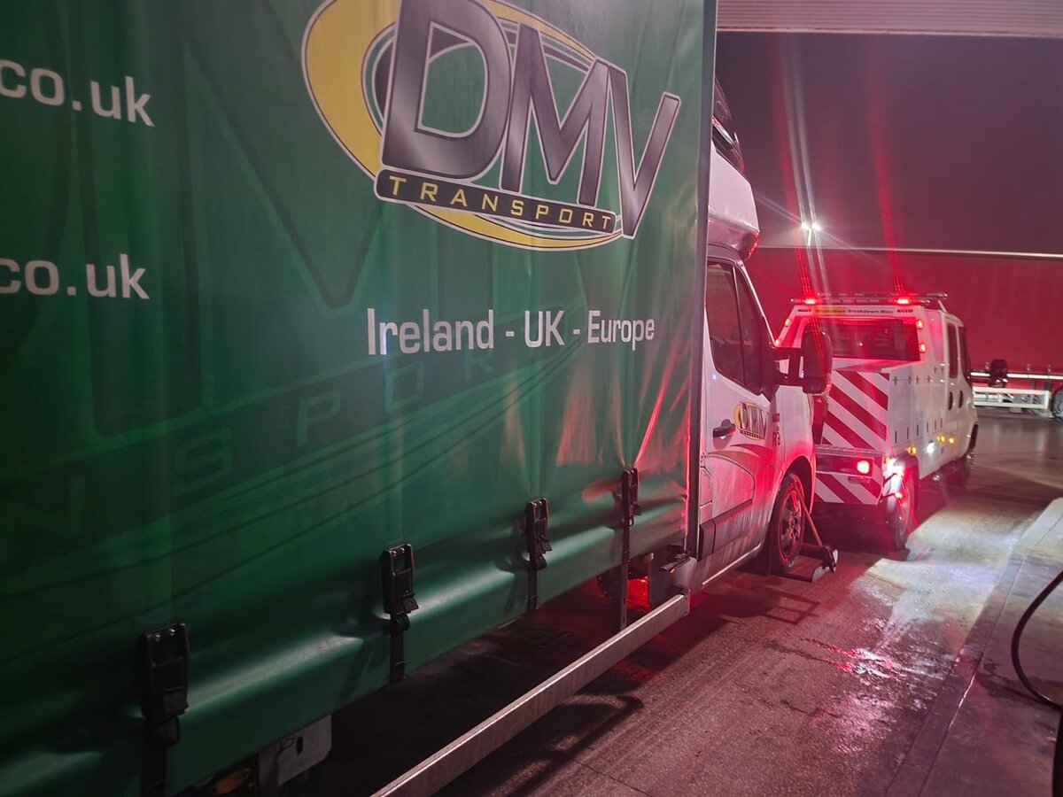 DMV Transport green curtainsider van being recovered by Breakdown Man's red rig under floodlight at night.