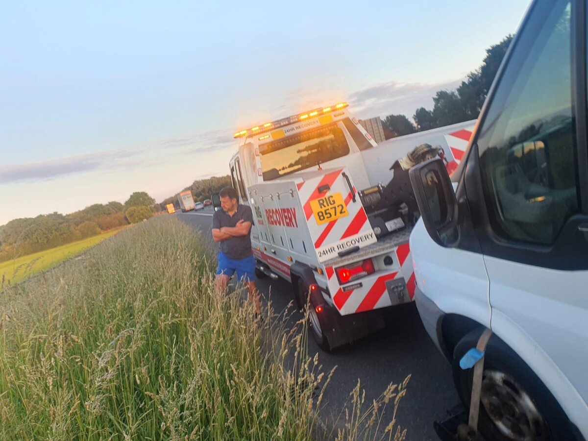 Two recovery trucks (RIG 8572) parked nose-to-tail on the motorway hard shoulder at sunset during a callout.