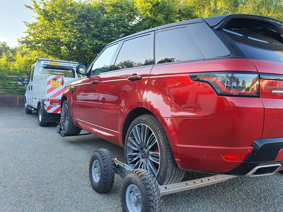 Red Range Rover Sport secured on a wheel-lift recovery dolly behind the Breakdown Man flatbed truck on a summer day at the depot.