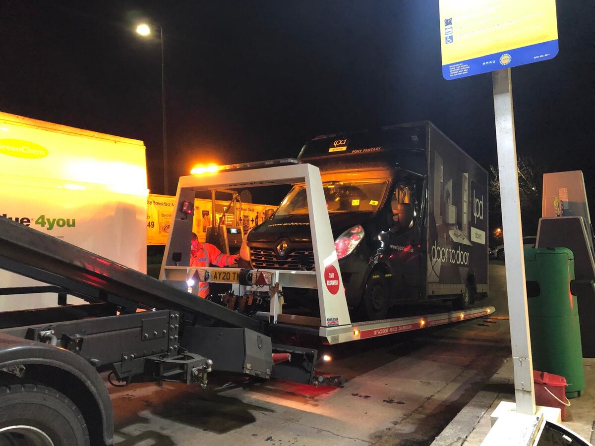 Courier van on a Breakdown Man flatbed leaving a petrol station forecourt at night after a wrong fuel call-out