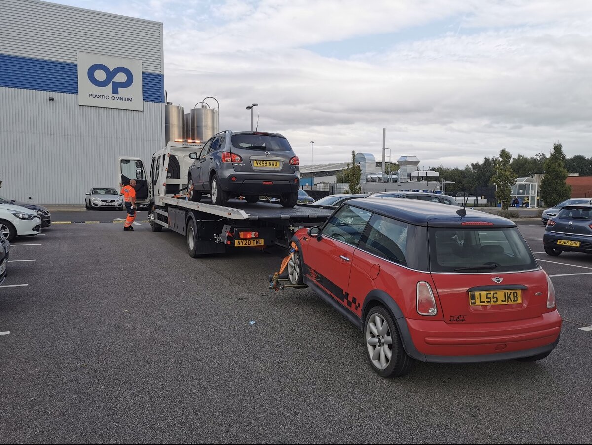 Silver Nissan Qashqai VK59 NAU loaded on the Breakdown Man flatbed AY20 TWU towing a red Mini Cooper L55 JKB outside the Plastic Omnium plant