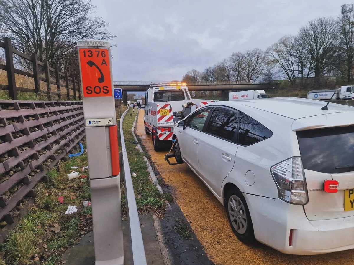 White Toyota Prius being recovered onto the Breakdown Man flatbed beside the SOS 1376A emergency phone on the M62 hard shoulder