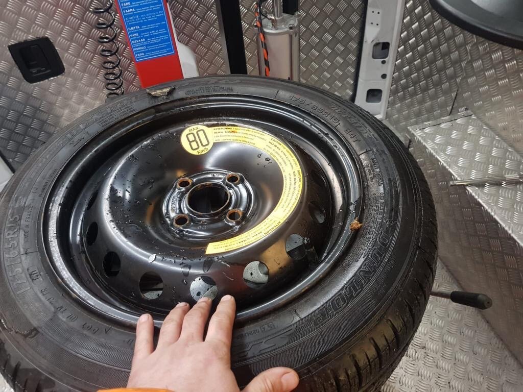 Punctured space-saver spare wheel laid on the chequered floor of a Breakdown Man recovery van during a roadside callout.