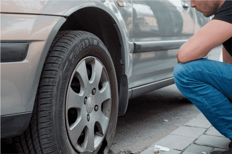 A person kneels to look at a flat car tyre.